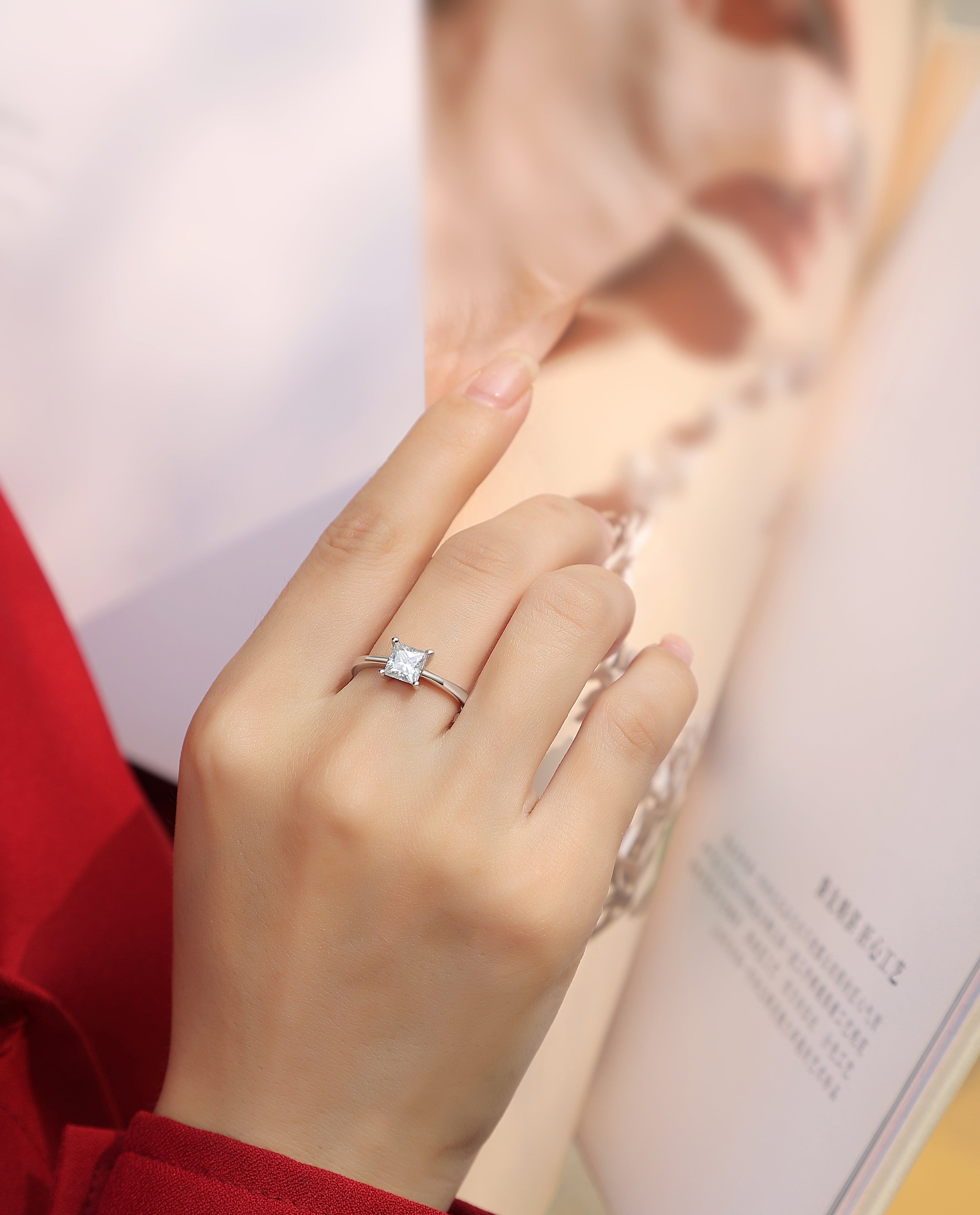 Elegant moissanite solitaire ring by Olivia Star Jewelry, princess cut stone set in 925 sterling silver, shown on hand in lifestyle photo with fashion magazine