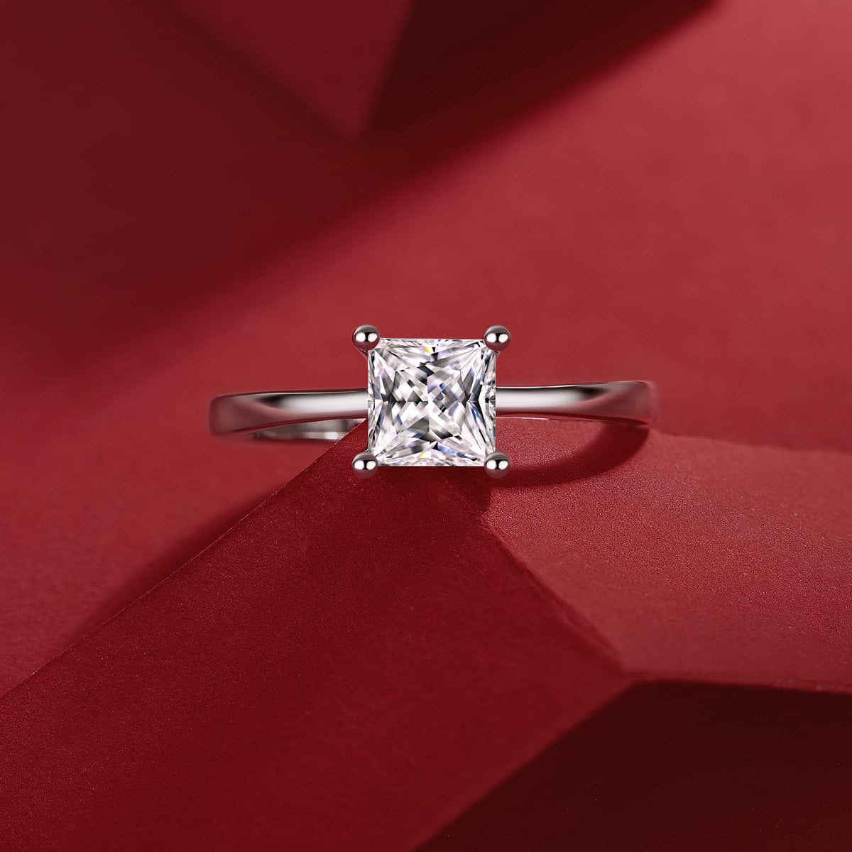 Elegant moissanite engagement ring, princess cut, solitaire design in 925 sterling silver, luxury jewelry by Olivia Star Jewelry, photographed on red background