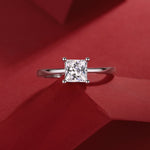 Elegant moissanite engagement ring, princess cut, solitaire design in 925 sterling silver, luxury jewelry by Olivia Star Jewelry, photographed on red background