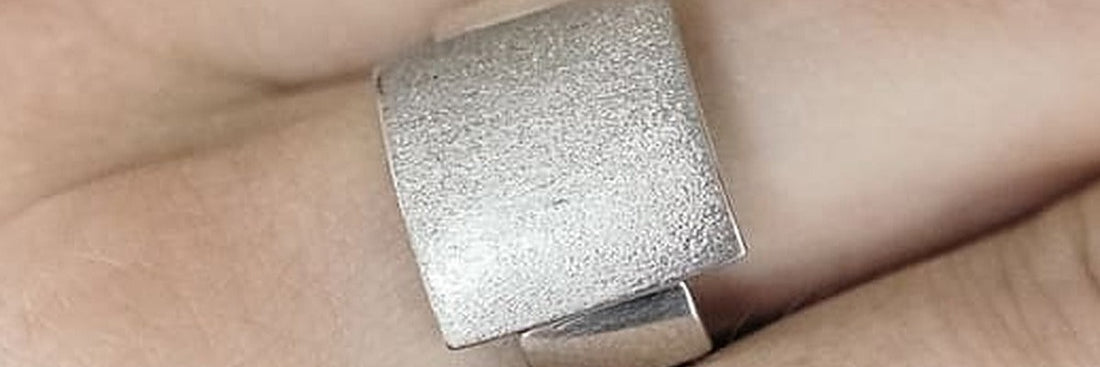Sterling silver ring with a brushed plate worn on a hand