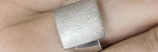 Sterling silver ring with a brushed plate worn on a hand