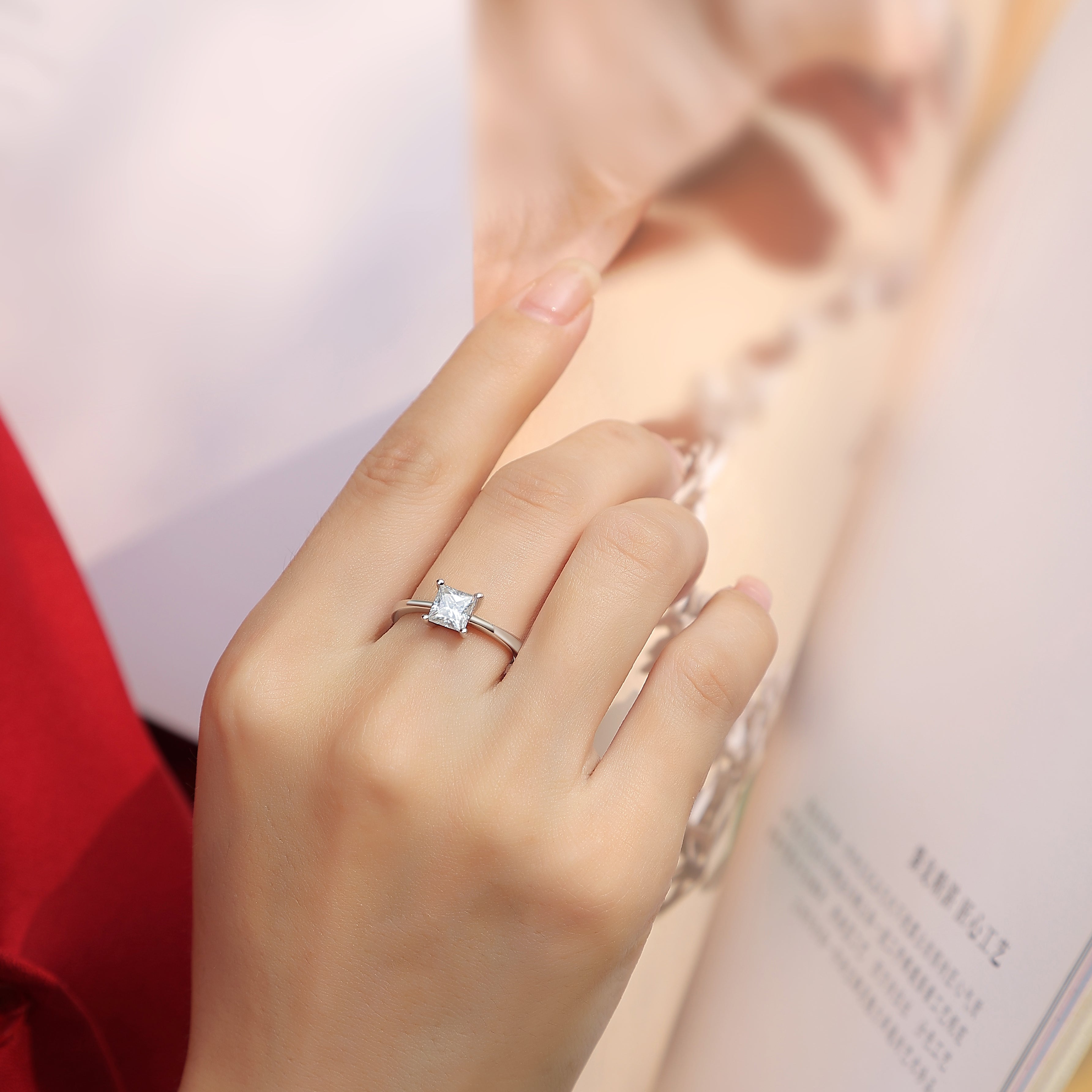 Elegant moissanite solitaire ring by Olivia Star Jewelry, princess cut stone set in 925 sterling silver, shown on hand in lifestyle photo with fashion magazine